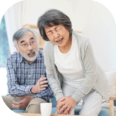 ソファーから立ち上がろうとして膝の痛みを堪えるばあばと心配そうに手を差し伸べるじいじの様子